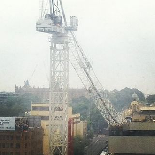 A low-quality photo of a building crane, the derrick of which has slumped onto a building core