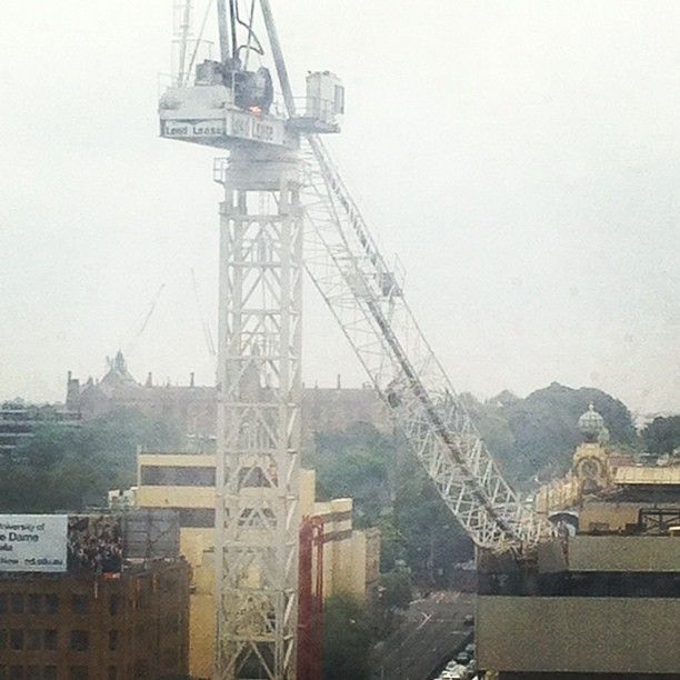 A low-quality photo of a building crane, the derrick of which has slumped onto a building core